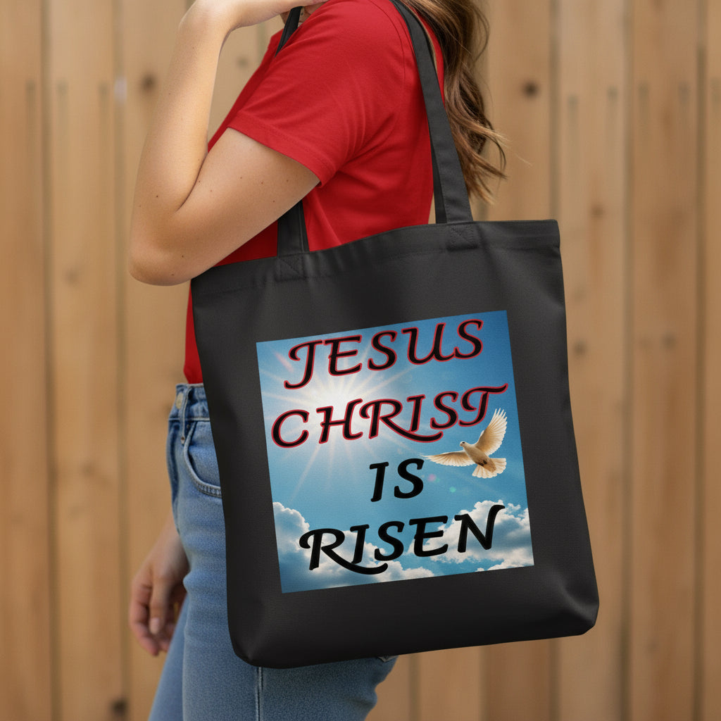 Person holding a black tote bag with 'Jesus Christ is Risen' design.