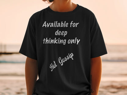 Person wearing a black t-shirt with text 'Available for deep thinking only. Not Gossip' at the beach.