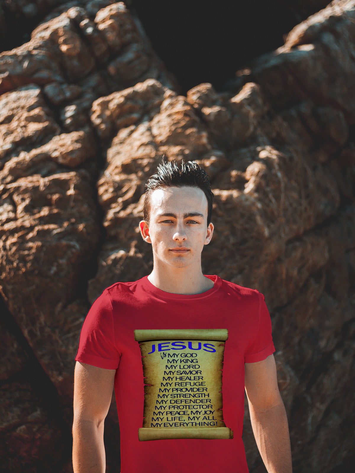 Person wearing a red t-shirt with 'Jesus' text design, standing in front of a large rock.